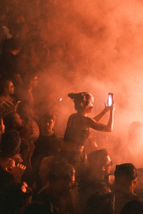 Girl sitting on shoulders recording with smartphone in golden smoke crowd